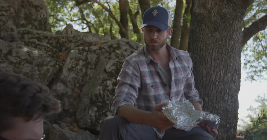 Two men eat outside under a tree