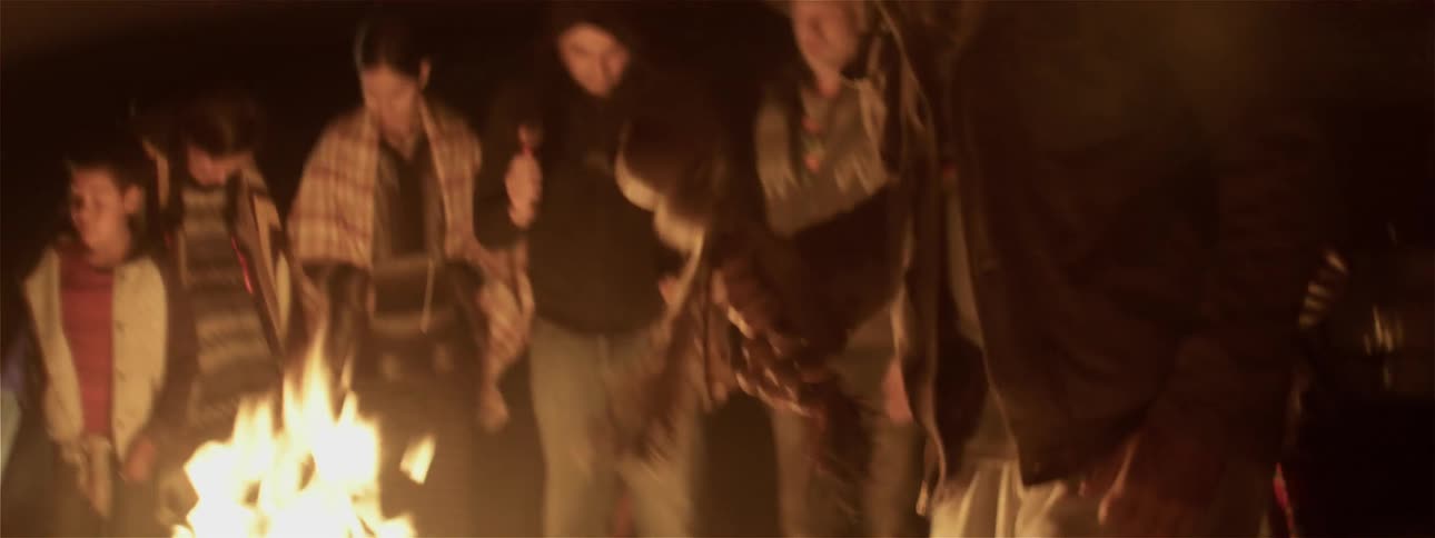 People dance and shake instruments by the campfire