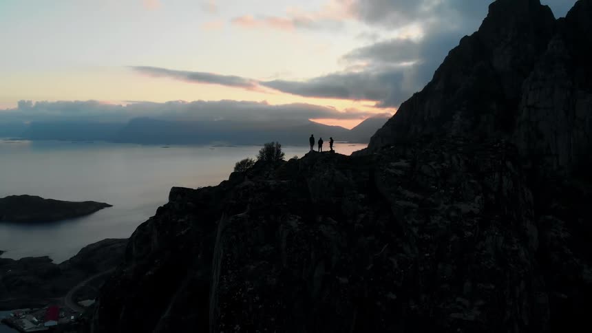 Three people are standing on a cliff at sunset