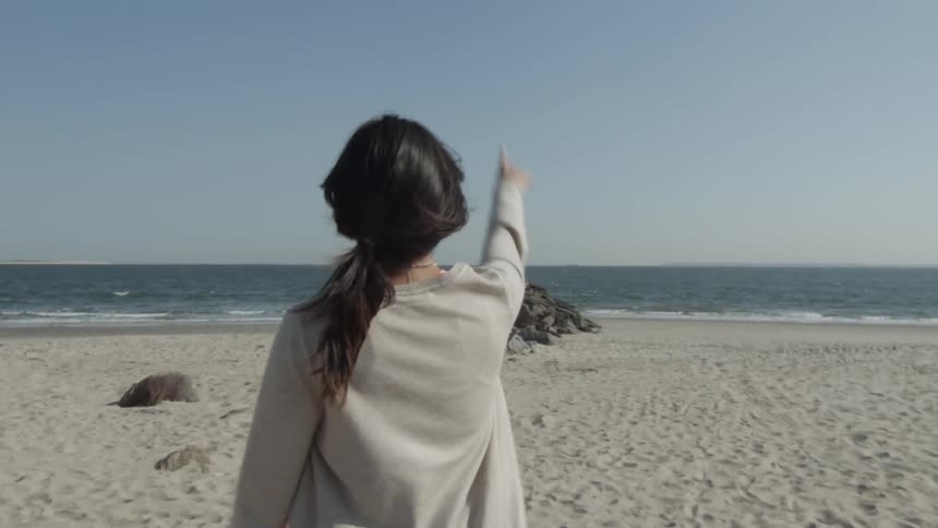 Woman walking down a beach points in the air