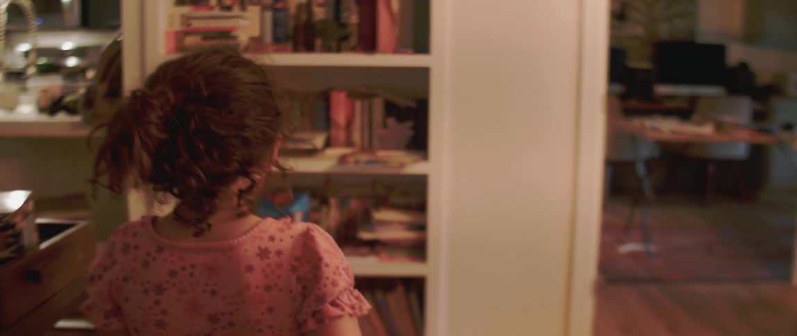 A young girl walks through a house towards a bookcase