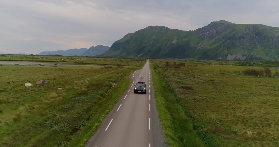 A car is driving down a road with two green fields on each side