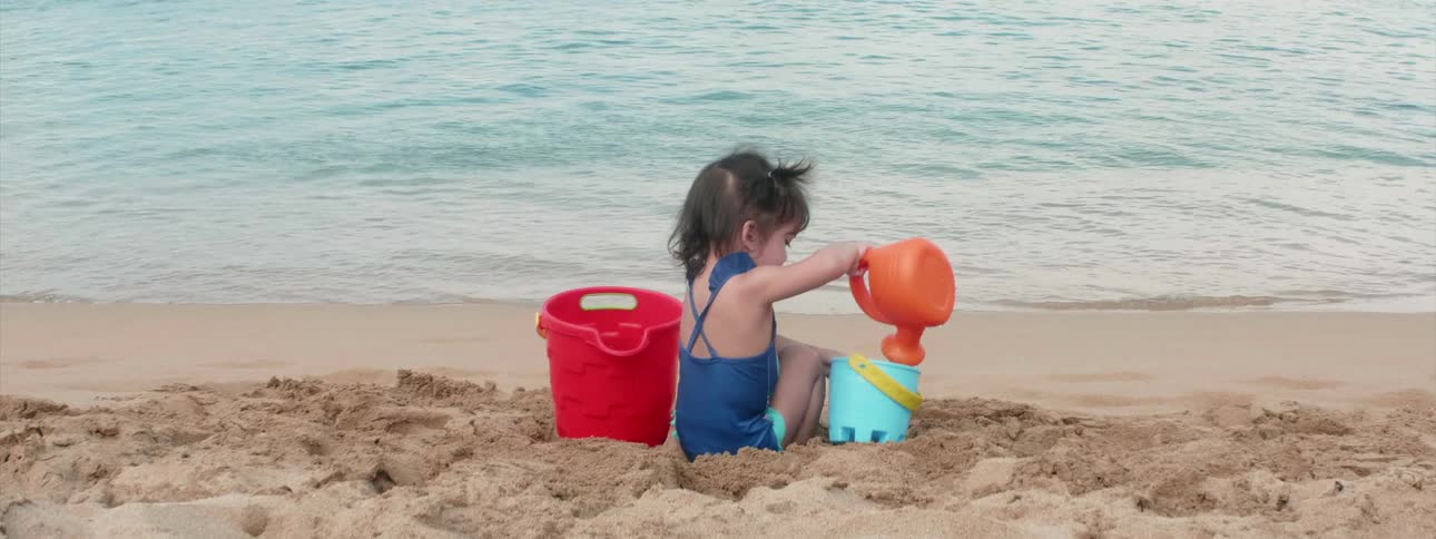 A girl plays in the sand at the water's edge