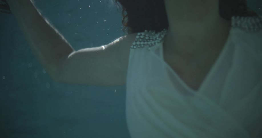 Woman wearing white dress swims to surface of water