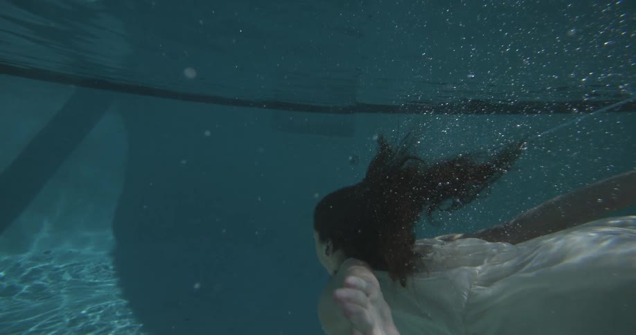 A dark haired woman swims in her pool