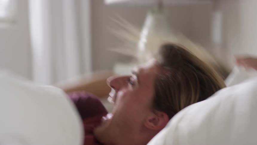 Man sleeping in bed woman hitting him with a pillow