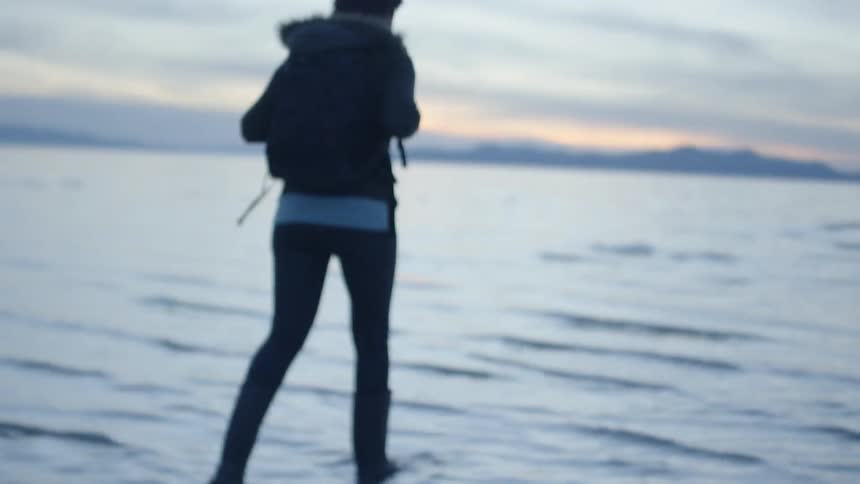 Woman wearing a jacket and boots walks into the lake