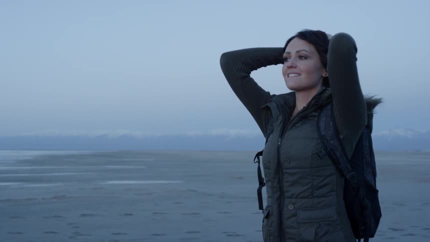 Woman puts hands on head while standing outside smiling