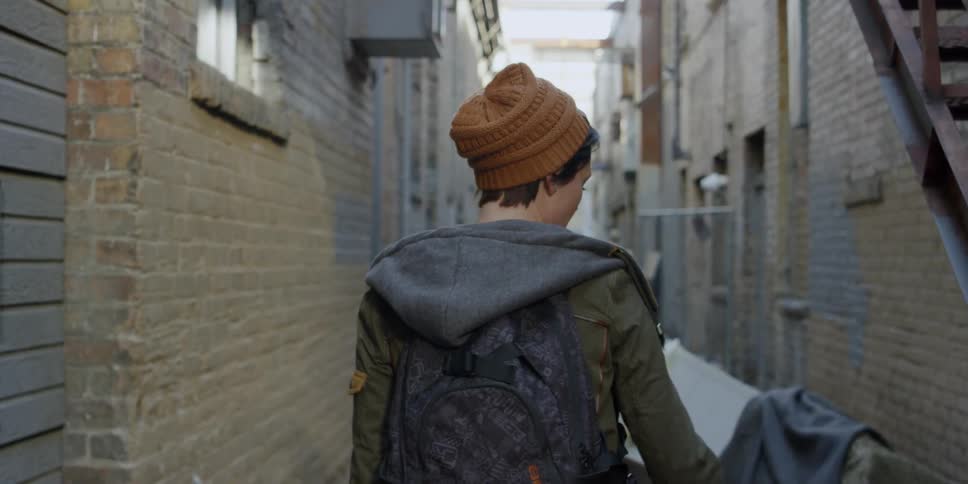 A woman is looking around as she walks through a city alleyway in daylight
