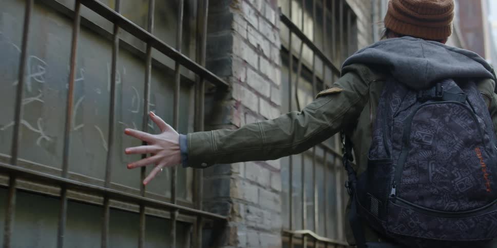 Woman drags her hand along the side of a building as she walks