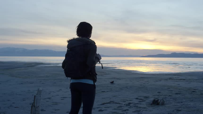 Woman stands on a beach at sunset