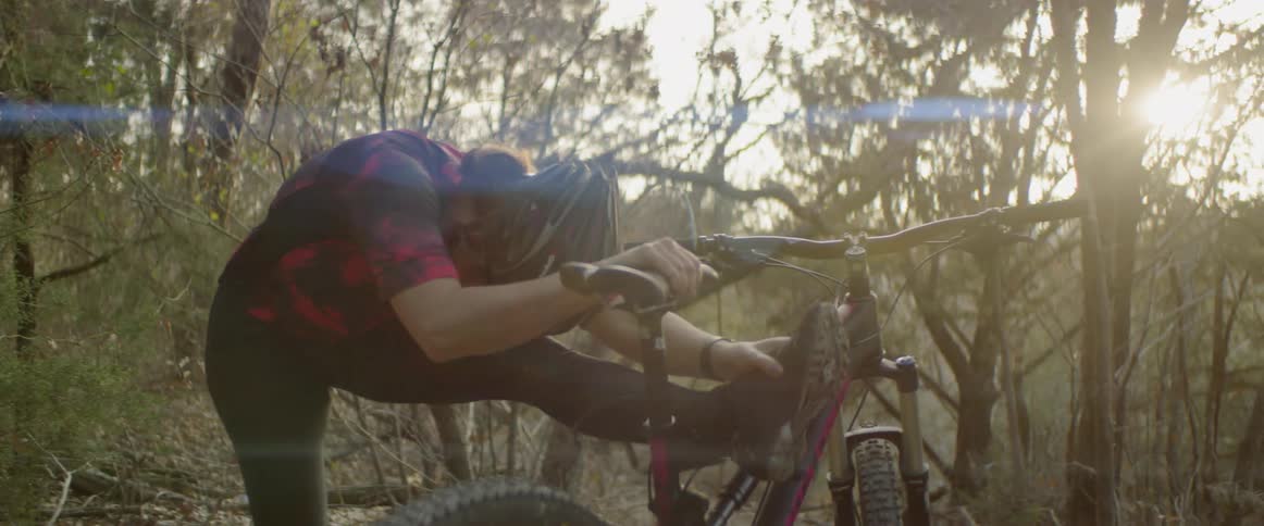Woman stretches leg while leaning on her bike in the woods