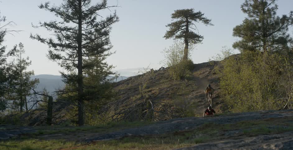 Two people ride bikes down a small hill