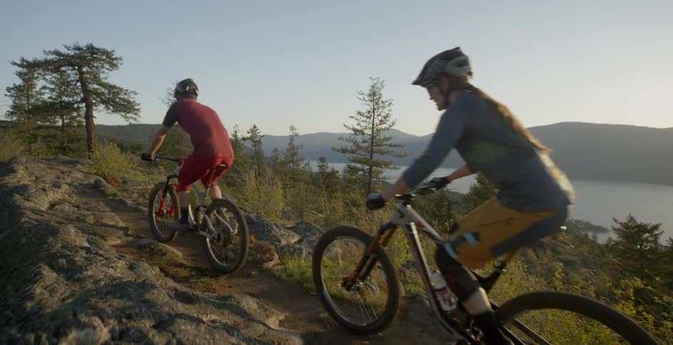 Two people ride mountain bikes on a rocky trail on a sunny day