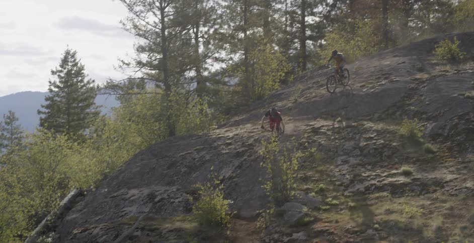 Two people ride mountain bikes down a rocky slope on a sunny day