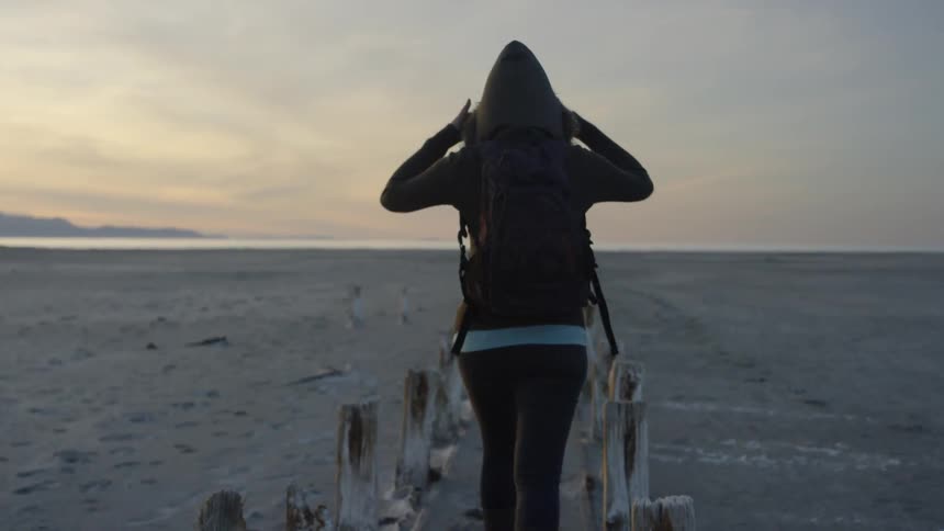 A woman walks onto the beach at sunset