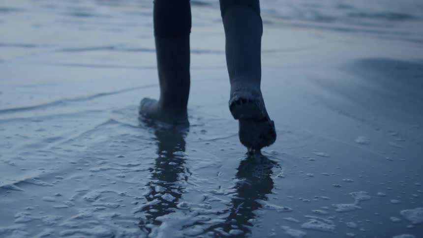 Person wades on a beach at sunset