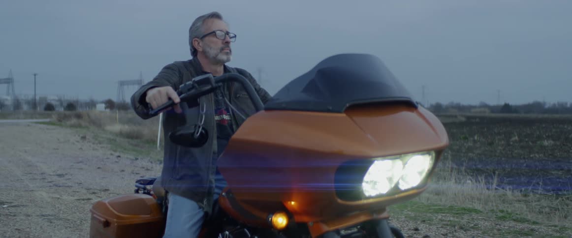 Man sits on an orange motorcycle outside in the country
