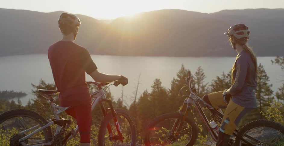 Two bikers stop and watch the sunset over a large lake