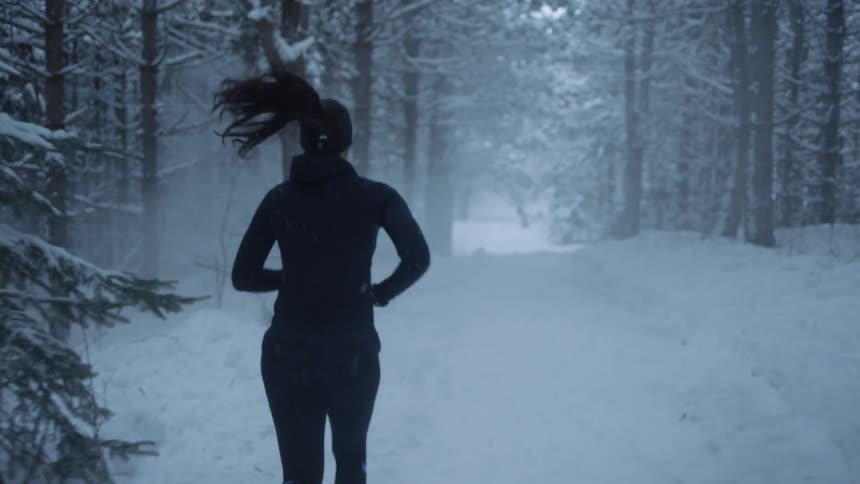 Woman jogging through the snow in forest