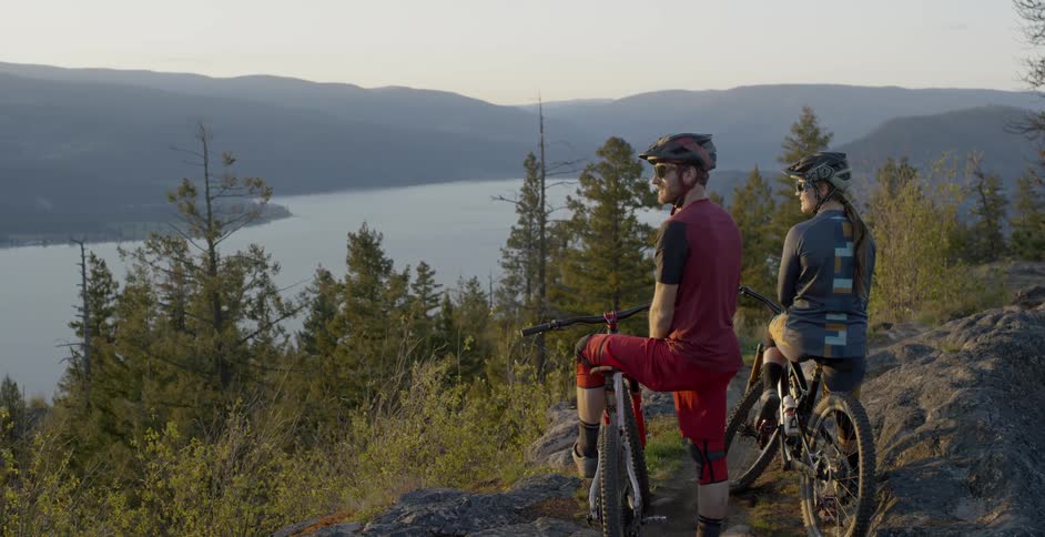 A man and woman sit on mountain bikes and look at the water below