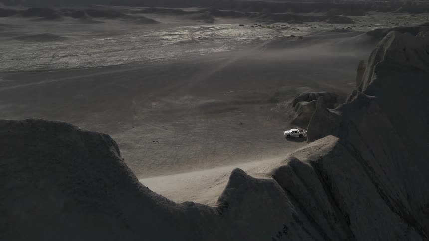 A pickup truck with a trailer hitched are parked at the base of a ridge