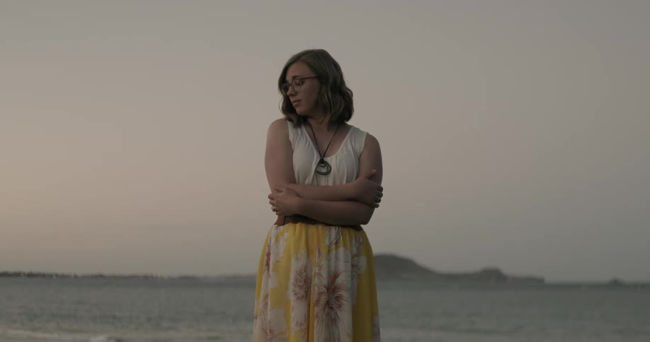 A woman looks around while hugging herself at sunset