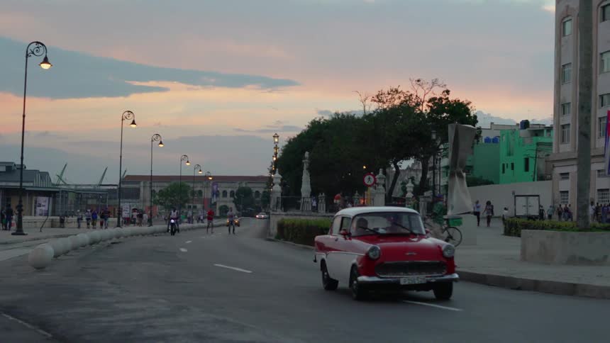 A classic car drives down a street through a town at sunset