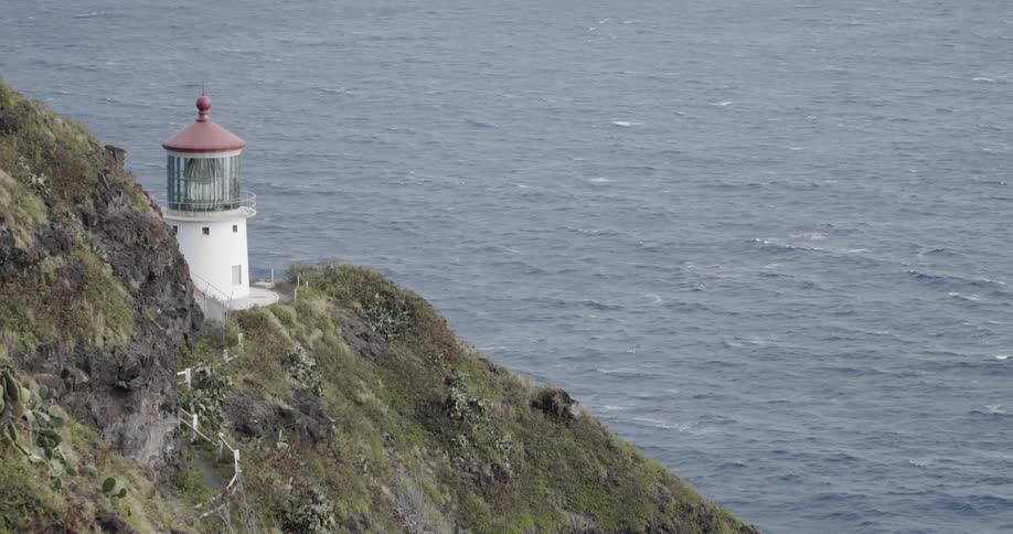 Lighthouse sitting on mountain side overlooking the ocean