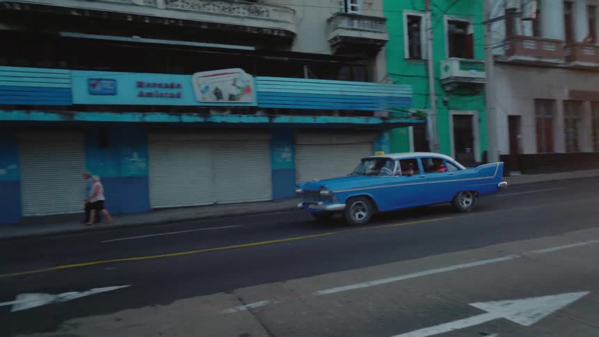 Blue car travels down the street past the buildings