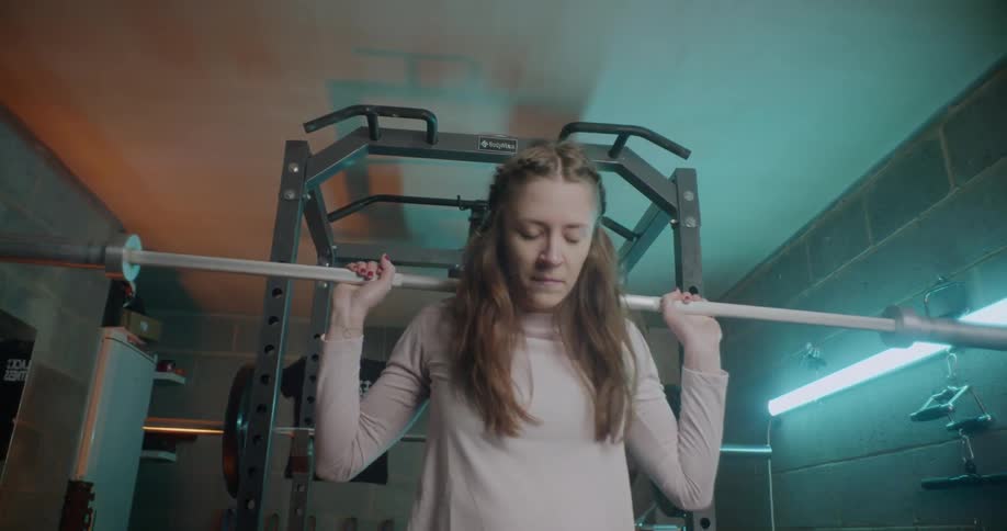 A woman is lifting a weight bar on her shoulders