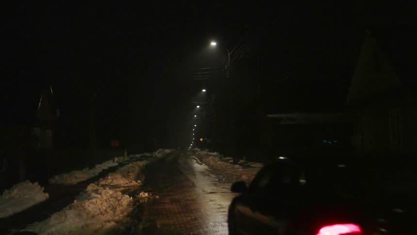A car drives on a snowy street at night