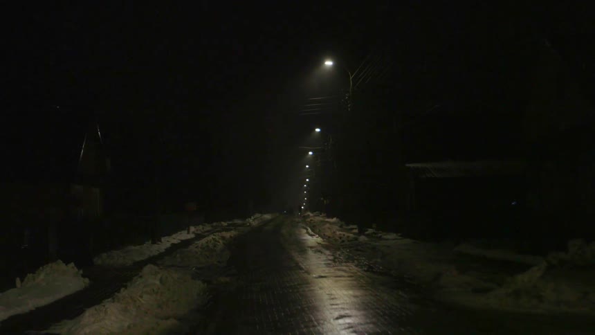 Street lamps shine on a snowy road