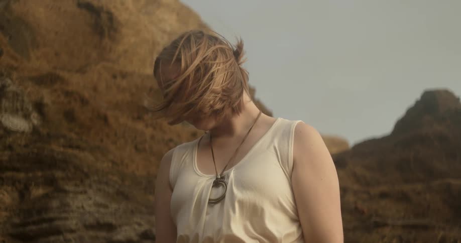 A woman is standing in the desert and the wind is blowing her hair around
