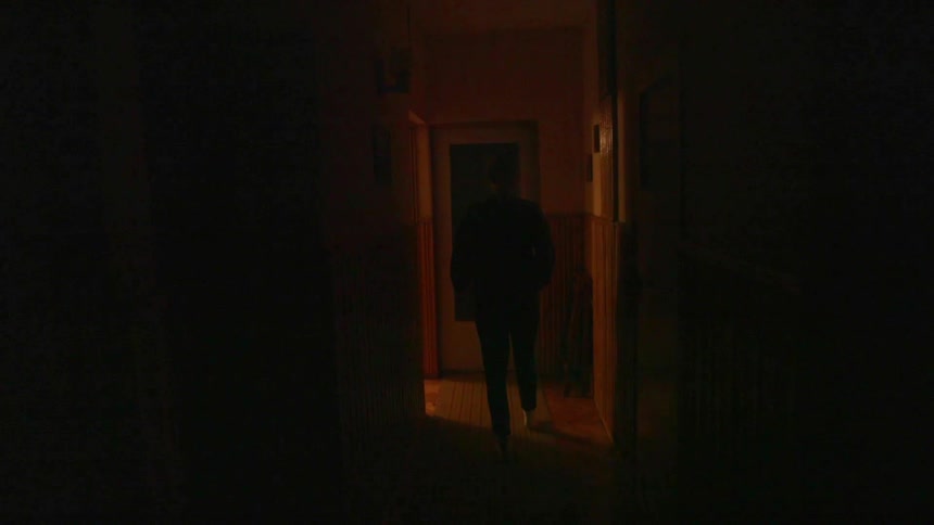 Woman walks down a dark hallway and then walks through a doorway