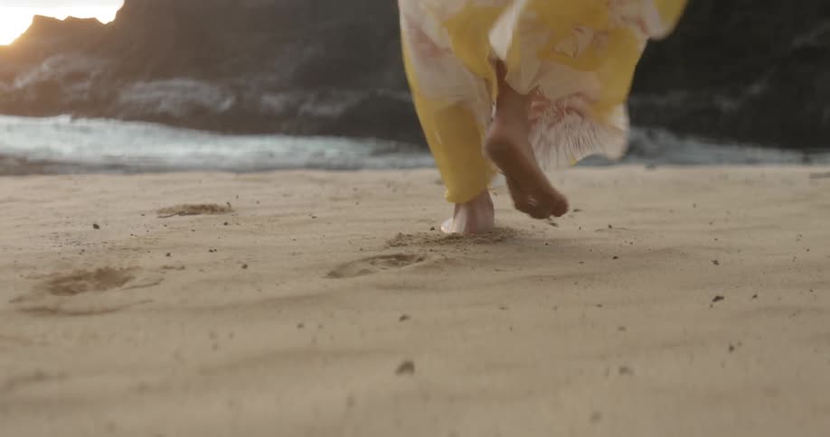 Woman walks on a windy beach at sunset