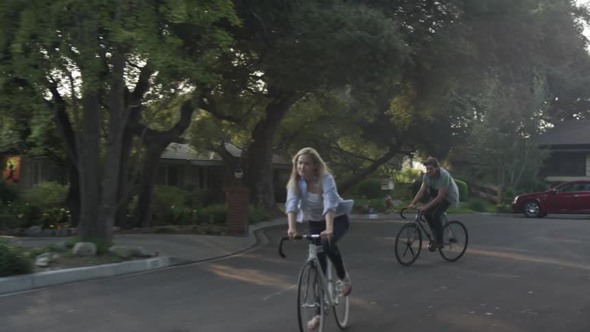 A man and woman riding their bikes through a neighborhood