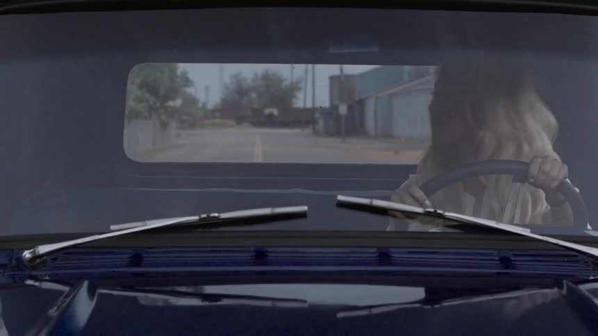 A woman sits in a truck as a man approaches from the back