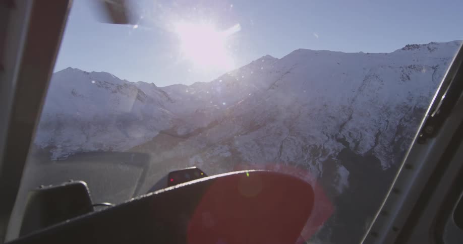 Man piloting a helicopter over a snowy mountain