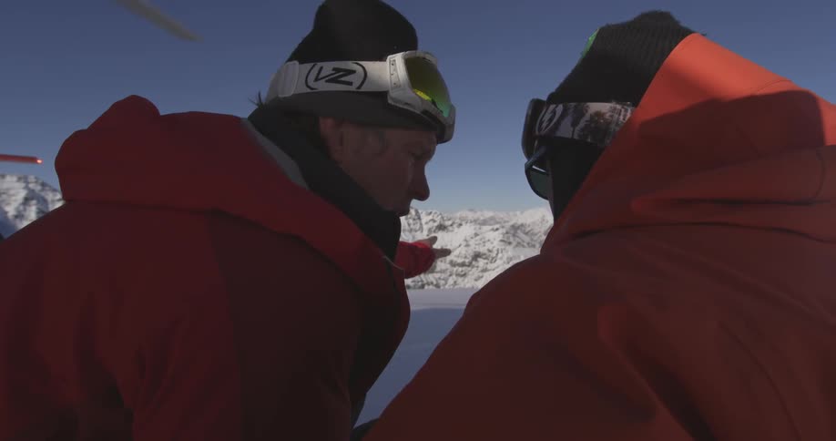 People talking on a snow covered mountain while helicopter blades spin above them