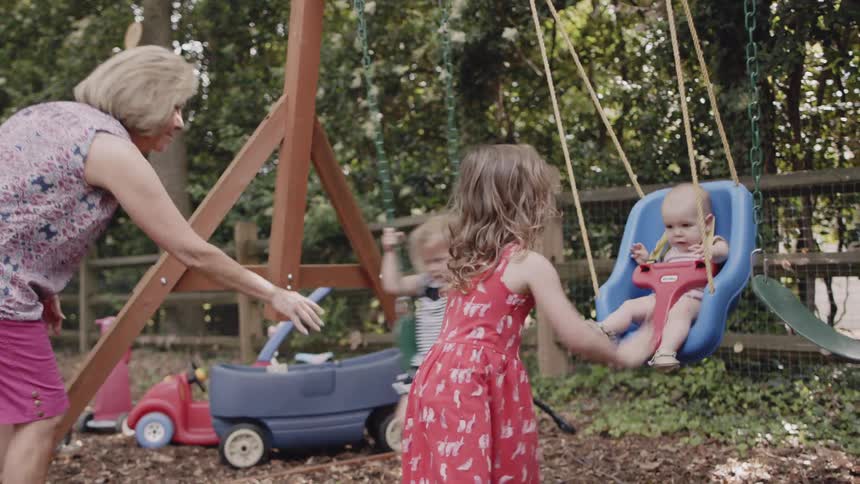 Woman pushes child on a swing and girl pushes a baby on a swing