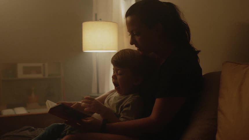 A woman is reading a book to her son who is in her lap
