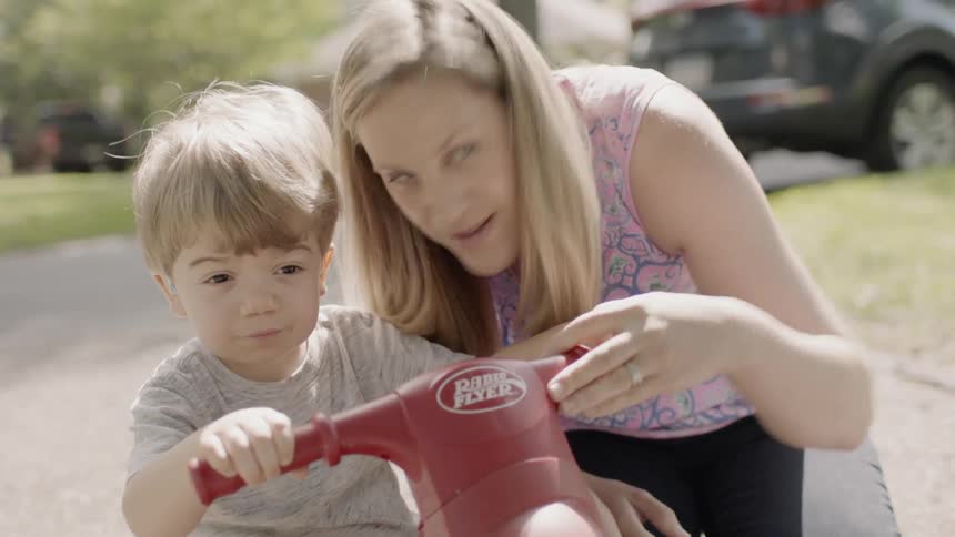 A mom talks to her son on a tricycle pointing to where he is going