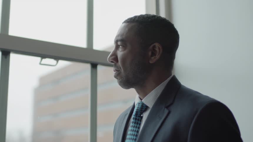 Man wearing a suit stands looking out a window