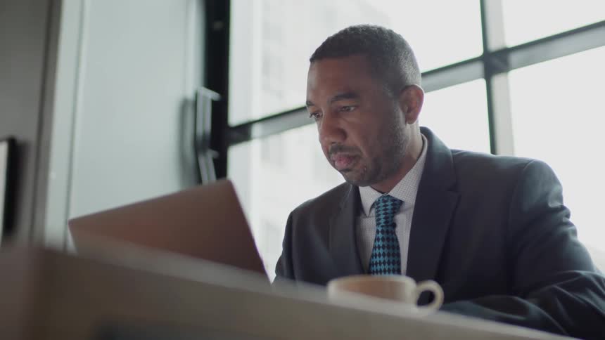 Man sits looking at a laptop near a window