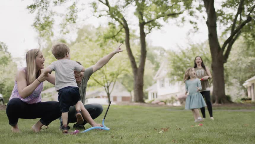 A mom and dad help their son launch a stomp rocket in the yard