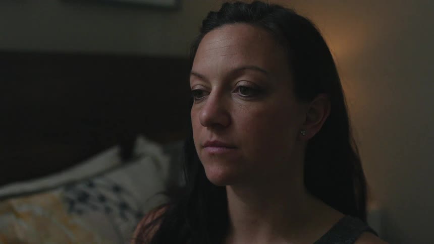 A woman is sitting on the edge of her bed looking at something