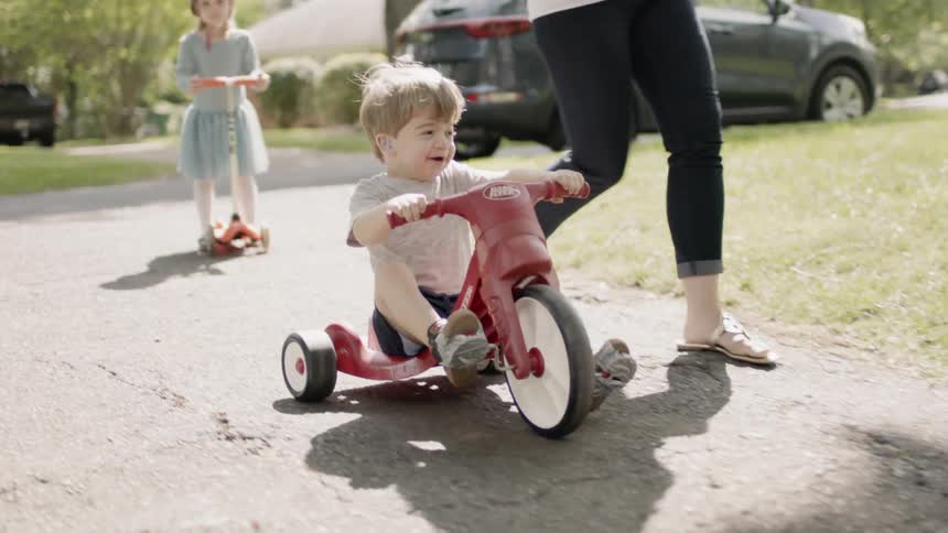 A woman pushes a young boy on a trike