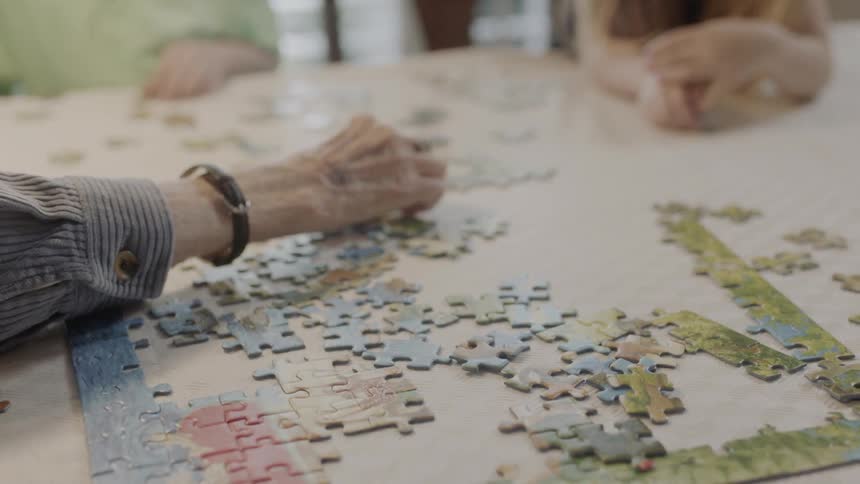 An elderly hand moves the jigsaw puzzle pieces on the table