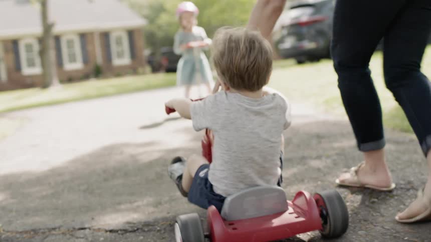A woman is helping a boy ride a tricycle outside during the day